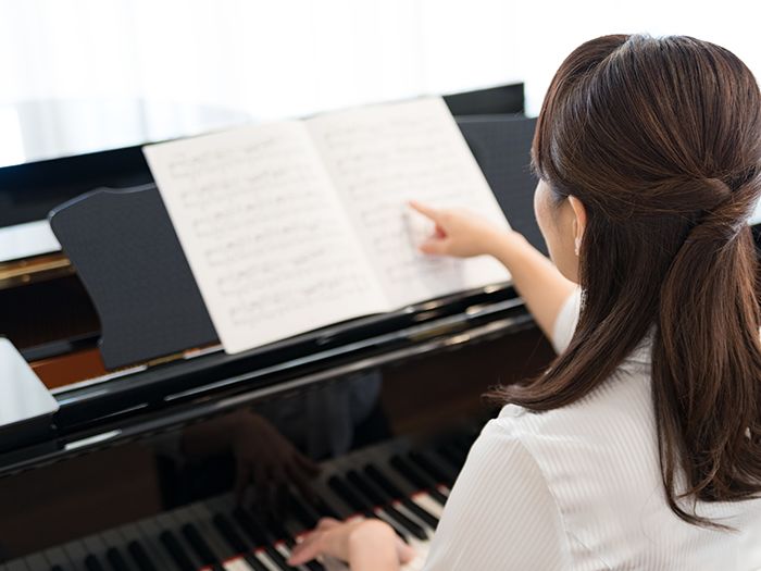 ピアノの前で楽譜を指さしている女性